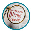 Magnifying glass viewing the words Government Hiring Freeze in a magazine.